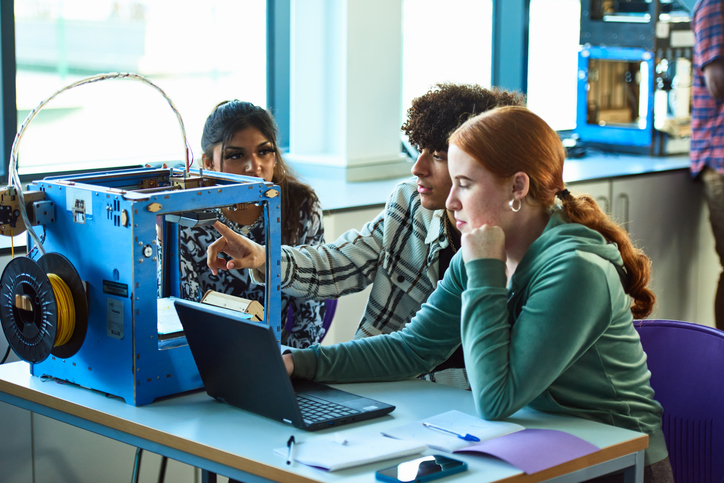 High school students collaborating on a STEM project using a 3D printer and laptop