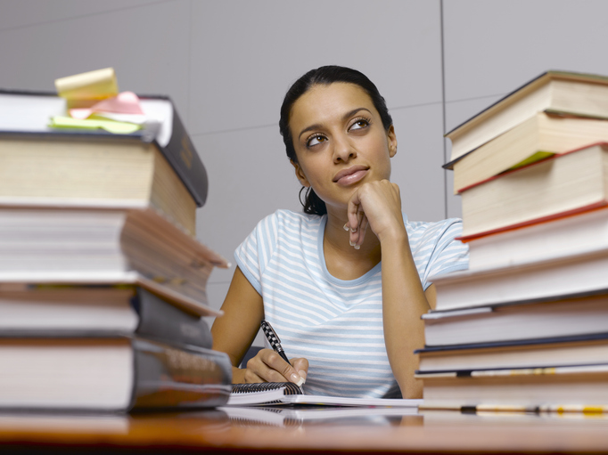 Is Communication a Good Major? A female student taking notes in a notebook surrounded by textbooks.
