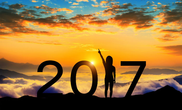 A graphic of a person standing on a mountain top looking at a beautiful orange sunset spelling out the numbers 2017