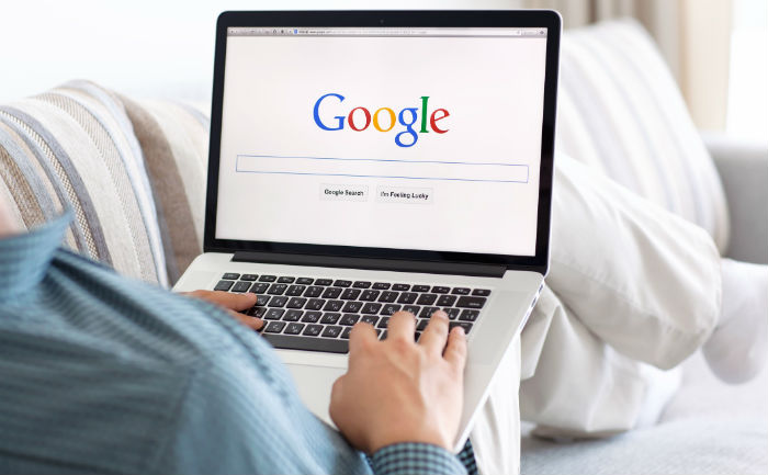 Person sitting on couch with laptop and looking at the Google browser before using Google Docs hacks.