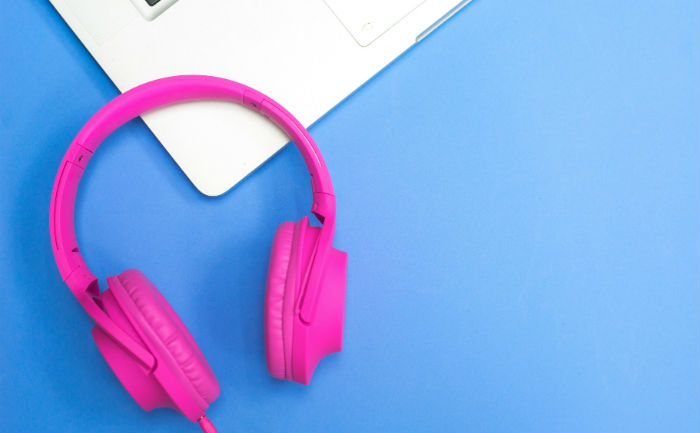 Bright pink headphones sitting on the edge of a laptop with a blue table underneath.