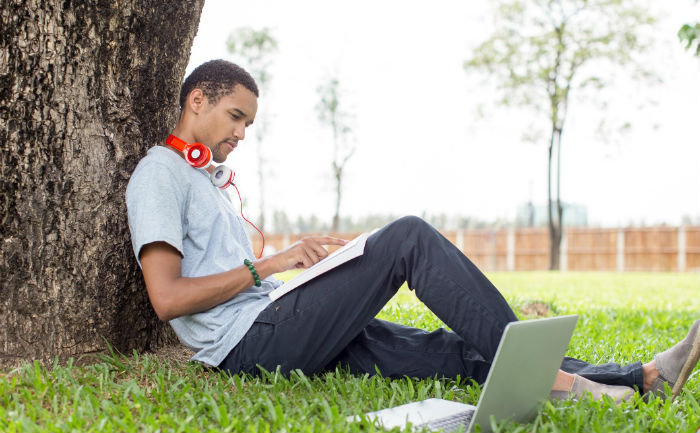  Young man sitting in the grass and leaning against a tree while learning how to improve study habits.