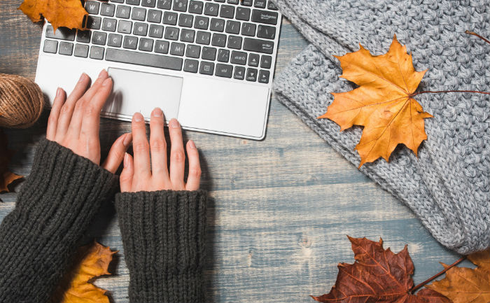 Person wearing a sweater and using silver laptop, surrounded by a gray blanket | How to be successful as an online student | UTEP Connect 