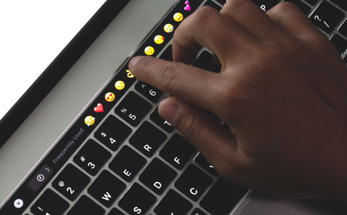 Close up of person’s hand touching emoticons on a keyboard.