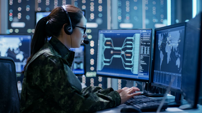 Female law enforcement officer monitors security threats using multiple computer monitors.