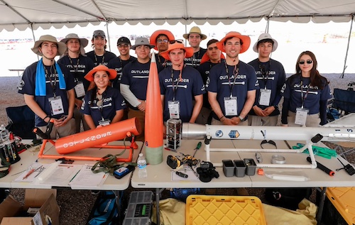 Members of the Sun City Rocket Team stand behind their rocket, Outlander, before final assembly. The team competed in the 2024 Spaceport America Cup at Spaceport America near Truth or Consequences, NM. 